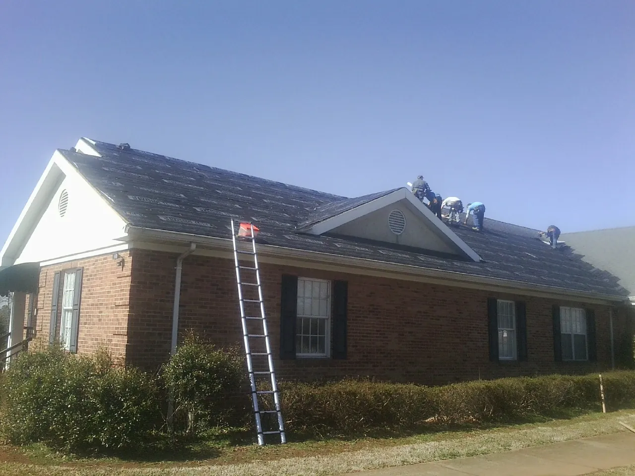 Crew tearing shingles off a brick ranch roof with a ladder set — Metal Roof Repair work by our crew in California