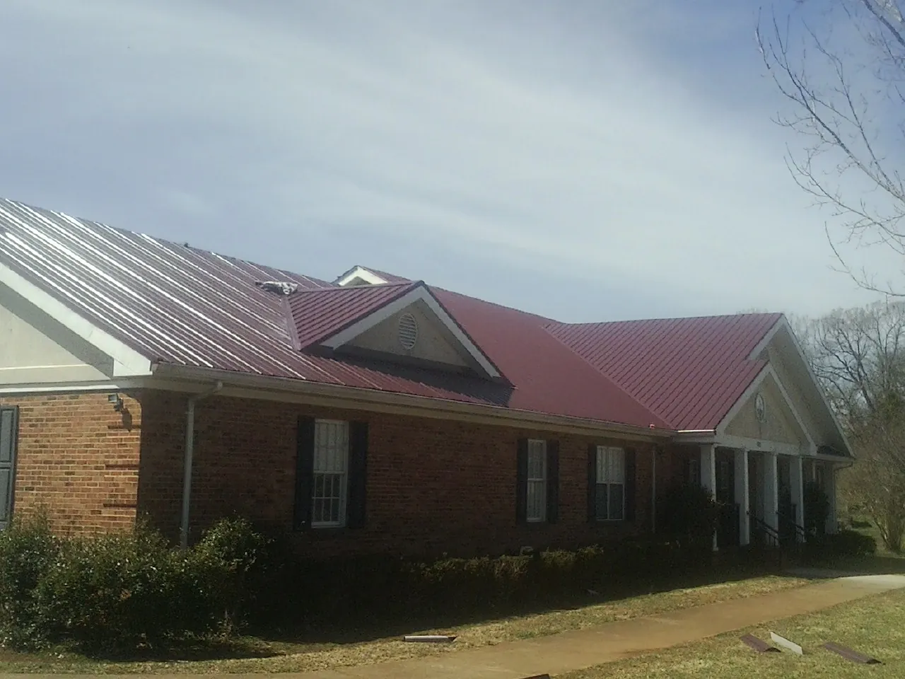Red metal roof with gabled entries on a long brick building, from a Hail Damage Roof Repair job in California