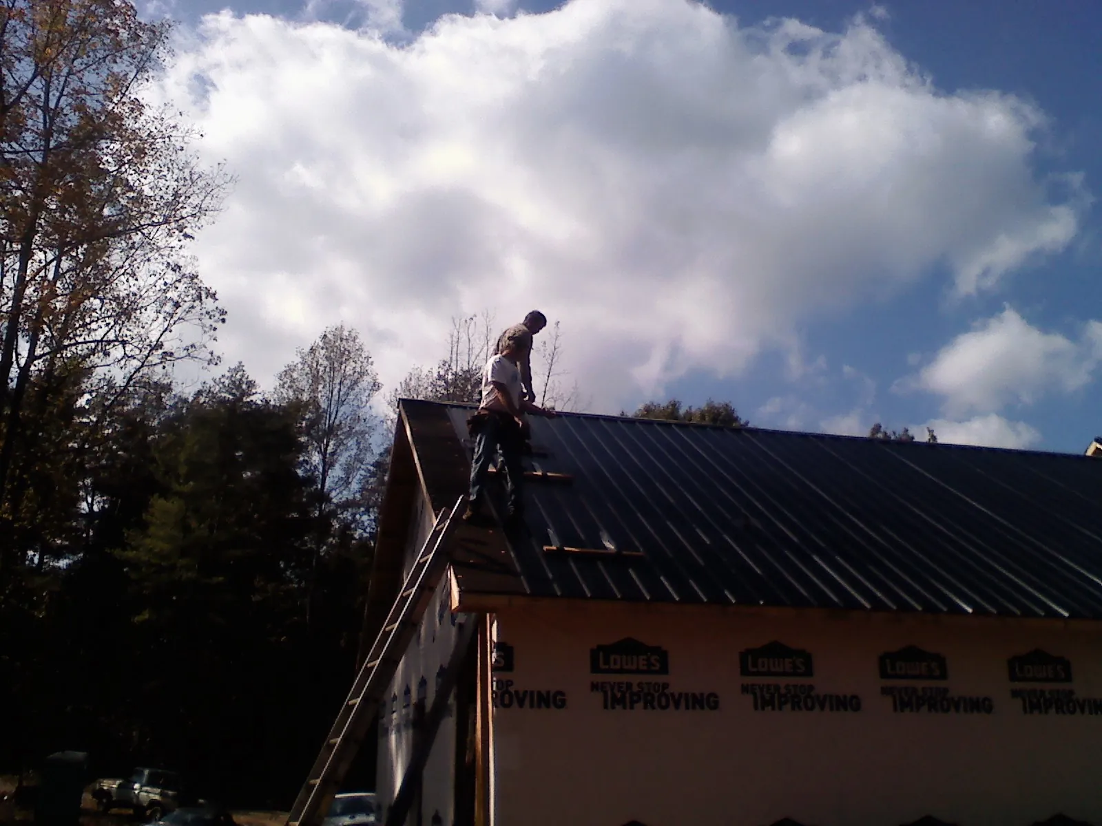 Roofer fastening dark metal panels high against a cloudy sky, from a Roof Inspection job in California