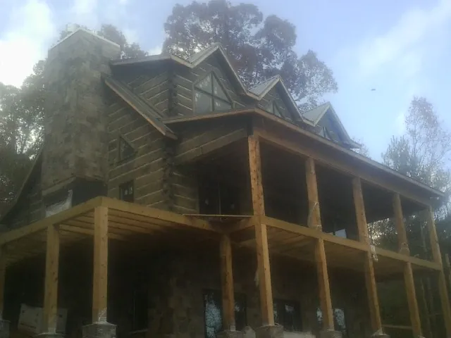 Stone chimney and dormers on a large log home with a timber porch in California