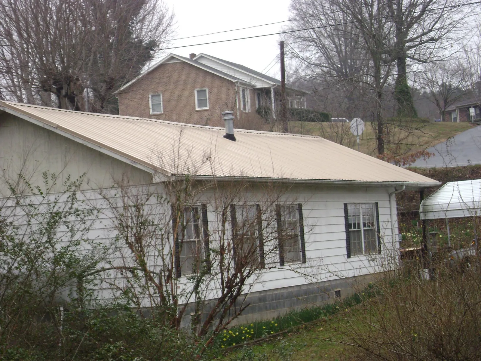 Tan metal roof on a white sided house set into a hillside — Commercial Roofing by Roofing Brothers in California